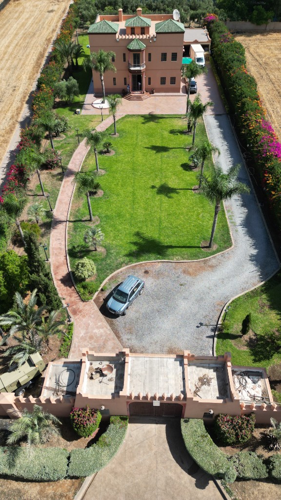 Vue aérienne d’une villa terracotta, allée gravillonnée et haies fleuries — drone Marrakech